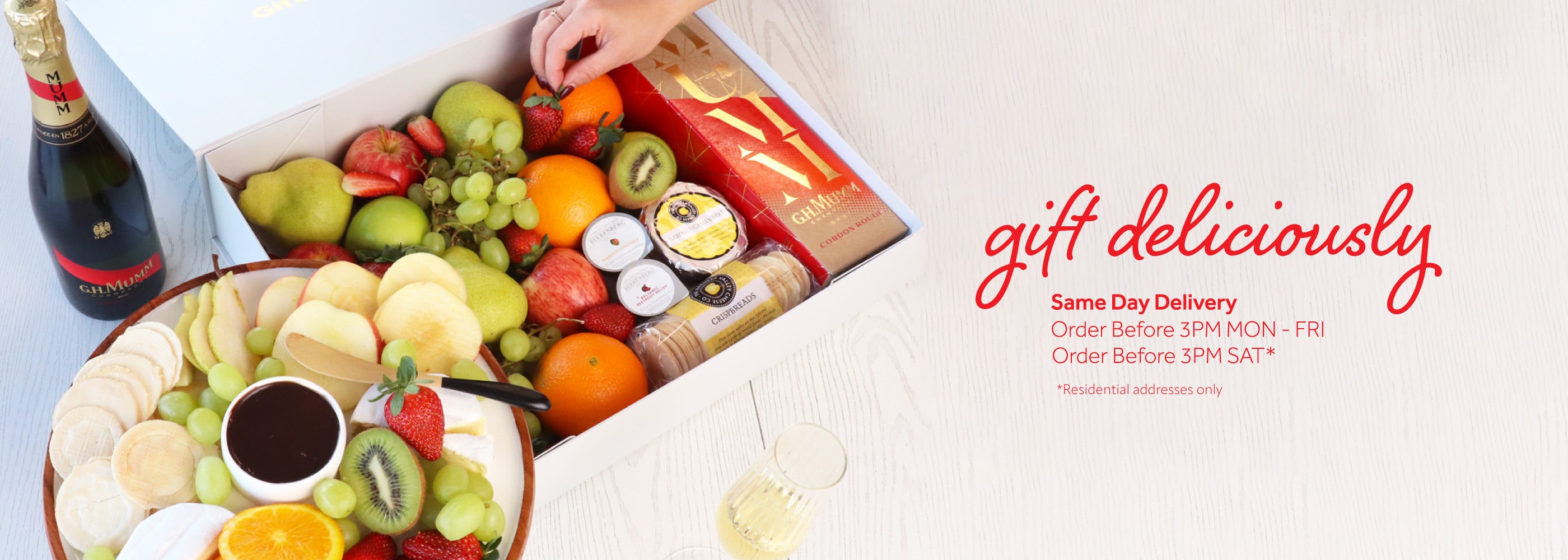 Gift box with fruits, chocolates, and a bottle of wine on a white background with 'gift deliciously' text.